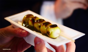 Dall’altra parte del mondo, i nostri ballerini addentano un aburi-mochi giapponese: tortine di riso grigliato in spiedini di bambù, una millenaria preparazione di Kyoto.